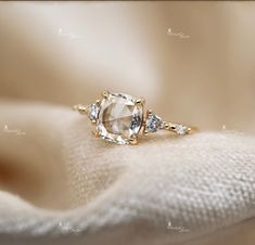 an engagement ring with three stones on top and two diamonds in the middle, sitting on a white cloth