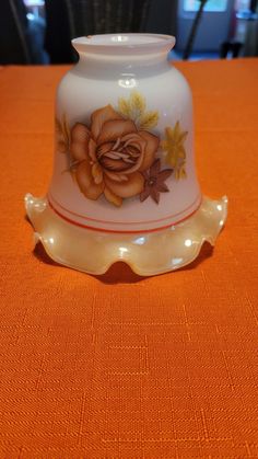 an orange table cloth with a white vase on it and a flower painted on the side