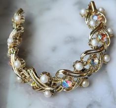 This very pretty 1950s gold tone bracelet is signed Coro on the fold over clasp.  It has aurora borealis rhinestones and imitation pearls in a swirled link design.  It is a small size measuring only 6 1/2" long and is in excellent condition with no wear or damage.   FREE SHIPPING within the USA and it will arrive gift boxed.    1038 Link Design, Bracelets And Charms, Aurora Borealis, Chain Link Bracelet, Pearl Bracelet, Vintage 1950s, Vintage Watches, Chain Link