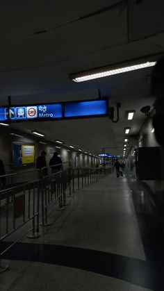 people are walking through an airport terminal with blue signs on the wall and lights above them