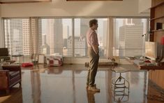 a man standing in front of a window looking out at the city outside his living room