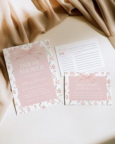 two pink and white wedding stationery cards on top of a bed with a beige drapes