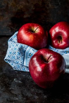 three red apples sitting on top of a blue cloth