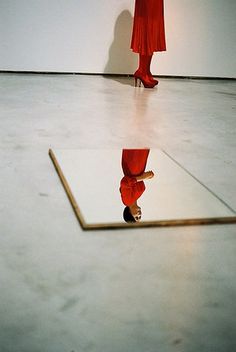 a woman's reflection in a mirror on the floor with her legs crossed and heels up