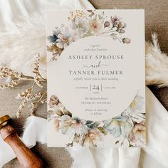 the wedding stationery is laid out on top of a white blanket with flowers and greenery