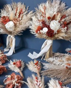 three bouquets of flowers and feathers are arranged on a blue surface with white ribbons