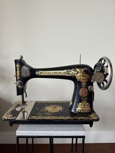 an antique sewing machine is sitting on top of a small table in front of a white wall