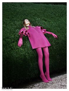 a woman laying in the grass with her arms and legs spread out, wearing a pink dress