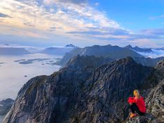 a woman sitting on top of a mountain next to a body of water in the distance