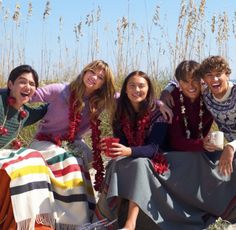 a group of young people sitting next to each other on top of a sandy beach