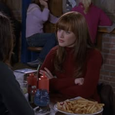 a woman sitting at a table in front of a plate of french fries with ketchup on it