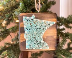 a wooden ornament hanging from a christmas tree with string art in the shape of a star