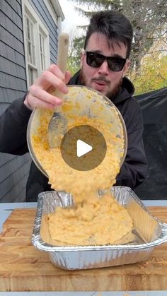 a man pouring cheese into a pan on top of a wooden table