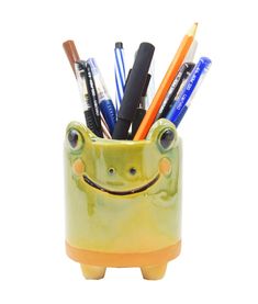 a green frog shaped pen holder with pens and pencils in it