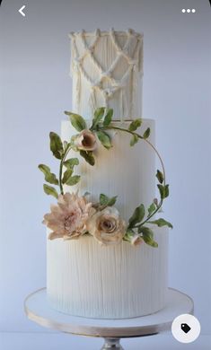 a three tiered white cake with flowers on top and greenery around the edges