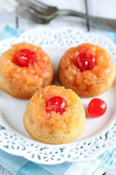 three pineapple upside down cakes on a white plate with cherries and a fork