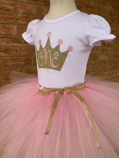 This birthday outfit is the most adorable way to celebrate her big day!This is a 2 piece set with either a bodysuit or shirt and a tutu. You can choose just the top, just the skirt or the outfit. Please choose carefully :)The top has puffed sleeves for super cute detail. It is embellished with a gold glittery crown with pink accents. A whimsical and enchanting ONE is spelled out in pink glitter. The tutu skirt has soft pink tulle with glitter strands throughout. A satin bow on top of the skirt c Gold Princess Tutu Dress With Ruffles, Princess Gold Tutu Dress With Ruffles, Princess Style Gold Tutu Dress With Ruffles, Princess Style Fitted Tutu Dress For Birthday, Tutu Birthday Outfit, Pink And Gold First Birthday, Smash Cake Outfit, Cake Outfit, First Birthday Tutu