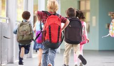 several children with backpacks are walking down the sidewalk