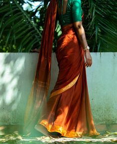 a woman in an orange and green sari leaning against a wall with palm trees behind her