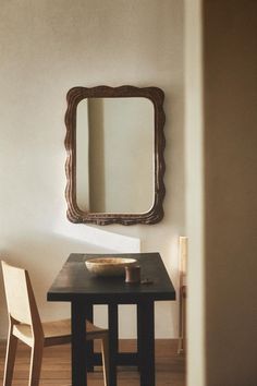 a small table with a bowl on it in front of a mirror and two chairs