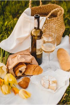 bread, wine and flowers on a blanket in the grass