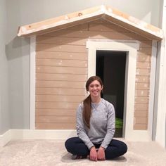 a woman sitting on the floor in front of a dog house that is being built