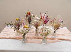 three vases filled with flowers sitting on top of a white table covered in pink cloth