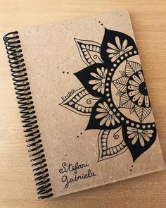 a spiral notebook with an intricate design on the front and back cover, sitting on top of a wooden table