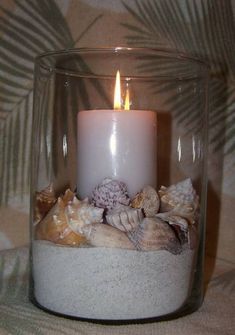 a candle that is sitting inside of a glass container with shells and sand in it