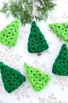 crocheted christmas tree ornaments hanging on a white doily with pine branches in the background