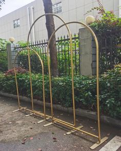 two golden metal arches sitting on the side of a road next to a tree and bushes