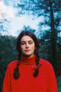 a woman with long hair wearing a red turtle neck sweater in front of some trees