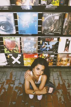 a woman sitting on the ground in front of a wall full of cds