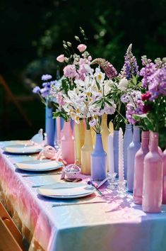 the table is set with pink and blue vases, plates, and wine bottles