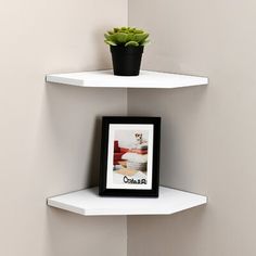 a white corner shelf with a potted plant on top and a black framed photo