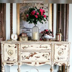 an old dresser with flowers on it in front of a painting and clock above it