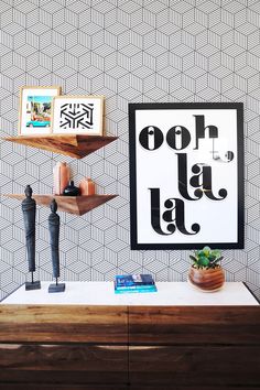 a wooden table topped with a shelf filled with books and vases next to a wallpapered wall