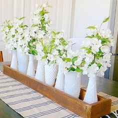 white vases filled with flowers sitting on top of a wooden tray next to a dining room table