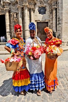 three women in colorful dresses holding flowers and baskets