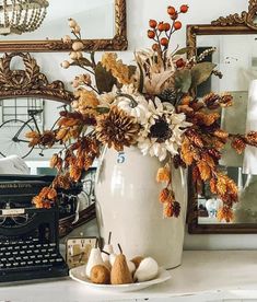 a white vase filled with lots of flowers on top of a table next to a typewriter