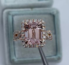 an engagement ring with a pink diamond surrounded by white and brown diamonds in front of a light blue box