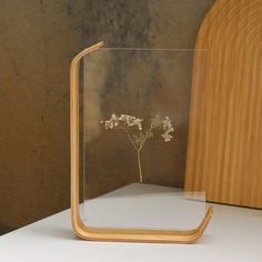 a glass vase with some flowers in it sitting on a white counter top next to a wooden frame