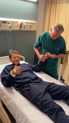 a man laying on top of a hospital bed next to an older man in scrubs