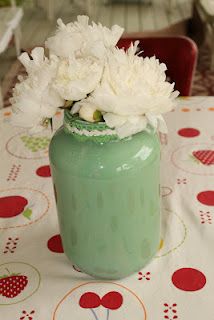 a green vase filled with white flowers sitting on top of a table covered in polka dots