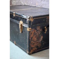 an old black trunk sitting on top of a cement floor next to a brick wall