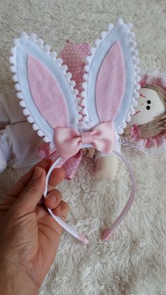 a hand holding a pink bunny ears headband on top of a white rug next to a stuffed animal