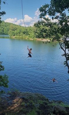 a man is jumping into the water from a high wire above his head and holding onto a rope