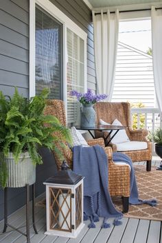 a porch with wicker chairs and potted plants on the front porch, covered by curtains