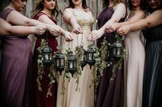 a group of women standing next to each other in long dresses holding small lanterns with greenery hanging from them