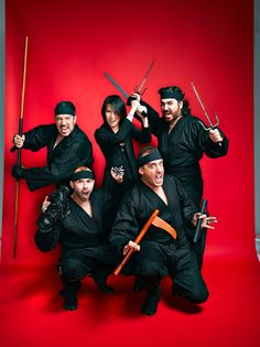 a group of ninjas posing for a photo in front of a red background with swords